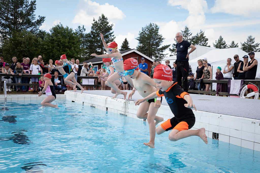 Flera barn hoppar i en pool från kanten.